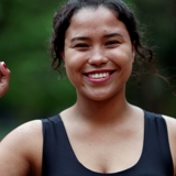 Photo of a young woman smiling, holding up her right hand in a fist.