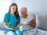 Photo of woman in scrubs sat on sofa with older woman holding cup of tea as they look at a chart together