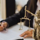 Justice statue and person in suit writing on paperwork