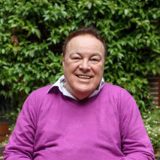 Photo of man in pink jumper sitting outside and smiling