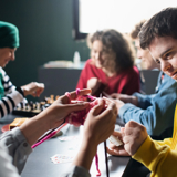 Photo of a group of people with learning disabilities doing arts and crafts projects, focused in on a young man, smiling. 