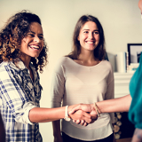 Two women meeting another woman (who has her back to the viewer), shaking hands and smiling.